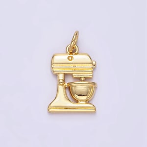 Pode incluir: Encanto de metal dourado em forma de batedeira de pedestal. O encanto tem uma tigela redonda e uma base com uma alavanca.