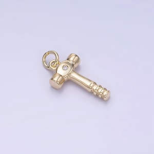 May include: Gold-toned hammer charm with a single clear rhinestone in the center of the hammer head. The charm has a loop at the top for attaching to a necklace or bracelet.