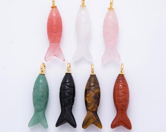 May include: A collection of seven carved fish pendants in various colors, including pink, white, green, black, brown, and red. Each pendant has a gold-colored bail for hanging.
