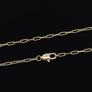 Op de afbeelding: Een goudkleurige ketting met een karabijnsluiting. De ketting is gemaakt van kleine, rechthoekige schakels. De ketting wordt gepresenteerd tegen een zwarte achtergrond.