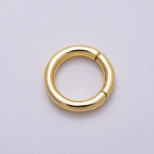 May include: A circular gold-toned metal ring with a smooth, polished finish. The ring features a visible hinge mechanism on one side, allowing it to open and close. The design is simple and continuous, showcasing a reflective surface throughout.