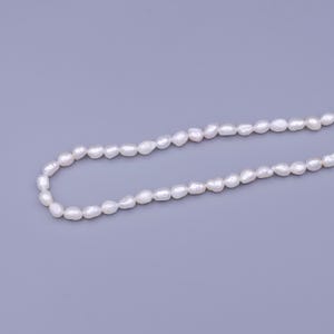 May include: A strand of white freshwater pearls, strung together to form a necklace. The pearls are oval-shaped and have a smooth, lustrous finish.