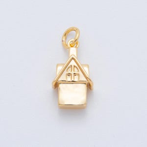 May include: A gold-colored house charm with a triangular roof and a rectangular body. The roof features a small window design. The charm includes a loop for attaching to a necklace or bracelet. The charm is made of a shiny, reflective material.