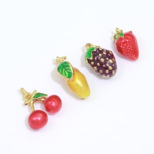May include: Four gold-tone charms shaped like fruit: a red cherry, a yellow mango, a purple blackberry, and a red strawberry. Each charm has a green leaf and a gold loop for attaching to a necklace or bracelet.