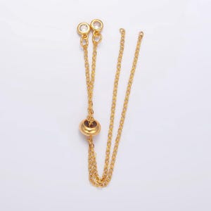 May include: Gold chain necklace with two clear crystal beads at the top and a gold bead in the center.