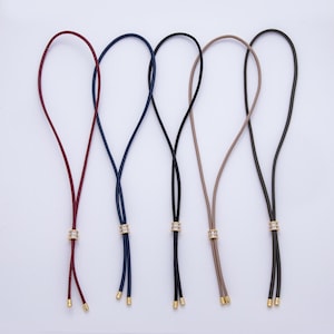 May include: Five eyeglass holders in various colors: burgundy, navy blue, black, tan, and dark olive green. Each holder features a decorative gold-colored band with clear rhinestones and gold-colored tips.