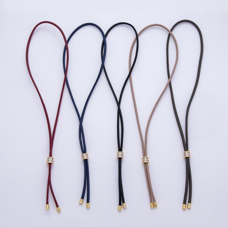 May include: Five eyeglass holders in various colors: burgundy, navy blue, black, tan, and dark olive green. Each holder features a decorative gold-colored band with clear rhinestones and gold-colored tips.