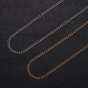 May include: Two chains, one silver and one gold, are laid out on a black surface. The chains are both made of small, linked circles.