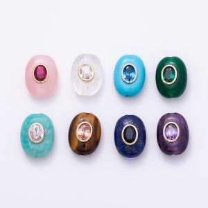 May include: Eight oval-shaped beads arranged in two rows. Each bead features a central faceted gemstone set in a gold-toned metal bezel. The beads come in various colors including pink, clear, turquoise, green, teal, brown, dark blue, and purple.