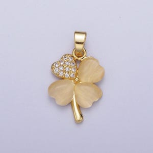 May include: A gold-tone pendant featuring a four-leaf clover design with a clear crystal center and white enamel leaves.