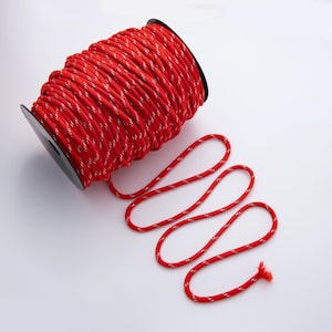 May include: A reel of red rope with a white reflective stripe. The rope is coiled on a black plastic reel, with a length of rope unraveled. The rope is a bright red colour and lies on a white surface.