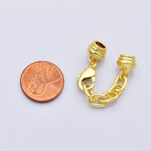 Puede incluir: Un cierre de joyer&iacute;a de color dorado con una cadena y un cierre de mosquet&oacute;n. El cierre est&aacute; al lado de una moneda de un centavo. El cierre tiene un dise&ntilde;o de barril texturizado en cada extremo. Los eslabones de la cadena tienen forma ovalada.
