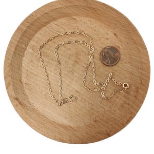 Op de afbeelding: Een gouden kettingketting op een houten oppervlak. Een cent is naast de ketting geplaatst ter vergelijking van de grootte.