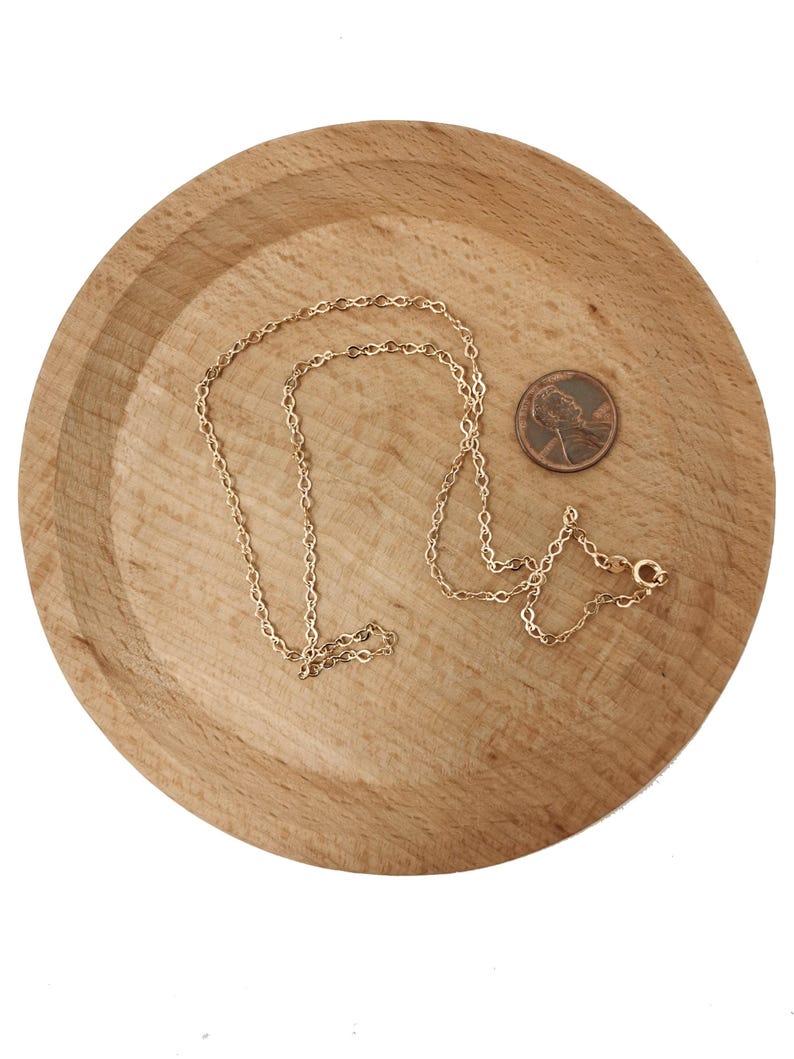 Op de afbeelding: Een gouden kettingketting op een houten oppervlak. Een cent is naast de ketting geplaatst ter vergelijking van de grootte.