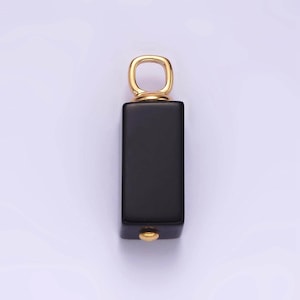 May include: A black rectangular pendant with a gold loop at the top. The pendant has a gold accent at the bottom.