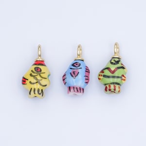 May include: Three colorful ceramic fish charms with gold-colored loops for hanging. The fish are painted in yellow, blue, and green with red, black, and white accents. Each charm has a unique design and shape.