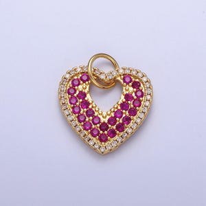 May include: A gold heart-shaped pendant with a small loop at the top. The pendant is covered in small pink and white gemstones.