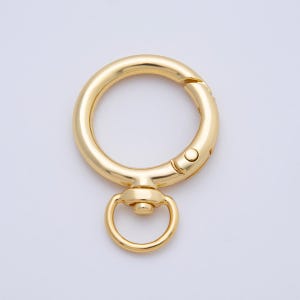 May include: A gold-colored swivel clasp with a circular ring and a smaller, attached ring. The clasp has a spring-loaded mechanism for easy opening and closing. The hardware is made of a shiny, metallic material.