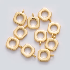 May include: A collection of gold-colored, geometric charms. Each charm has an octagonal shape with a circular opening in the center and a small loop at the top for attaching to jewelry. The charms have a shiny, metallic finish.