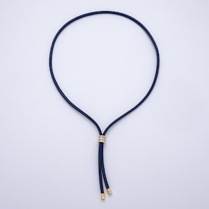 May include: A navy blue necklace with a gold-colored accent. The necklace has a circular design with a gold-colored ring at the center and gold-colored tips at the end of the dangling cords. The necklace is displayed on a white background.