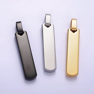 May include: Three metal pendant charms in black, silver, and gold. Each charm is rectangular with rounded edges and a small loop at the top for attaching to a chain.
