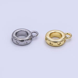 May include: Two metal charm beads. One is silver-colored, the other is gold-colored. Both are ring-shaped with a small loop and decorative cutouts. The beads are likely for jewelry making or crafting.