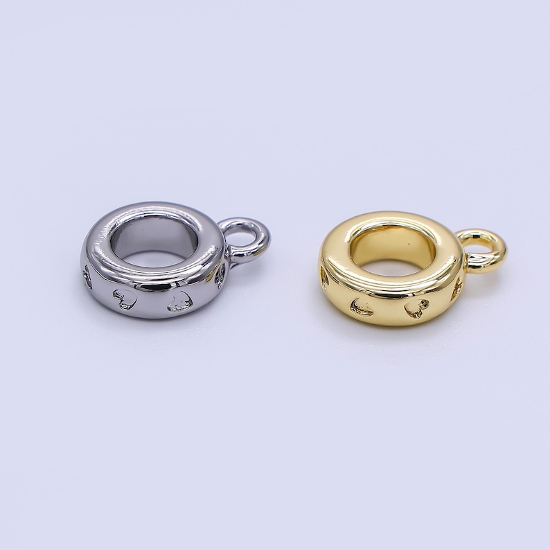 May include: Two metal charm beads. One is silver-colored, the other is gold-colored. Both are ring-shaped with a small loop and decorative cutouts. The beads are likely for jewelry making or crafting.
