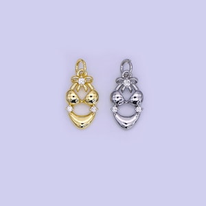 May include: Two bikini-shaped pendants. One is gold-colored, the other is silver-colored. Both have a bow at the top and are adorned with small, clear gemstones. The pendants are designed with a bikini top and bottom.