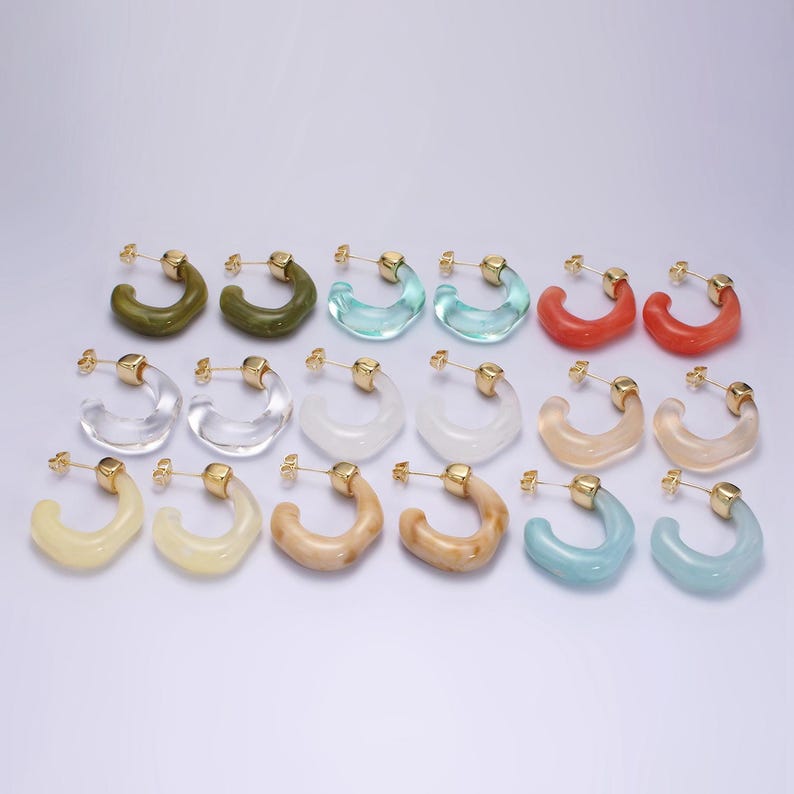 May include: A collection of hoop earrings in various colors, including green, blue, red, and clear. Each earring has a gold-colored post. The earrings are arranged in rows, showcasing their diverse hues and designs.