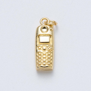 Puede incluir: Un dije dorado en forma de teléfono móvil vintage. El dije presenta una pantalla, botones y un lazo para sujetarlo a un collar o pulsera. El dije de teléfono es de un dorado metálico brillante.