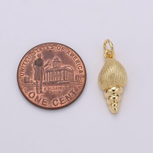 May include: Gold-toned seashell charm pendant with a textured surface and a spiral design. The charm is about the size of a UK penny.