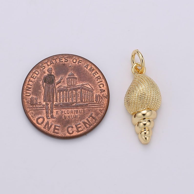 May include: Gold-toned seashell charm pendant with a textured surface and a spiral design. The charm is about the size of a UK penny.