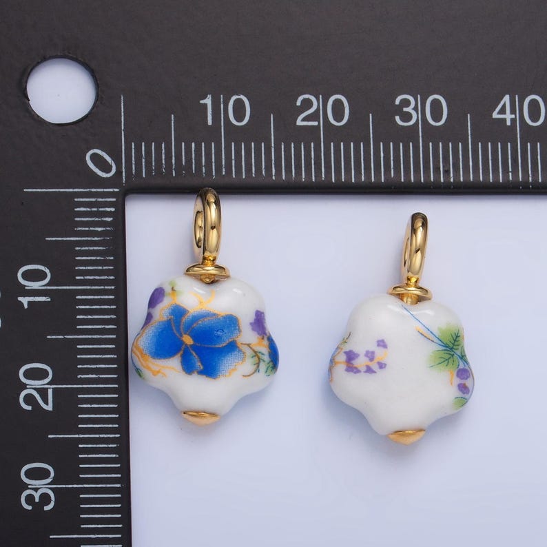 May include: Two white porcelain charms with gold accents and floral designs. The charms are shaped like a flower and have a gold loop for attaching to a necklace or bracelet.