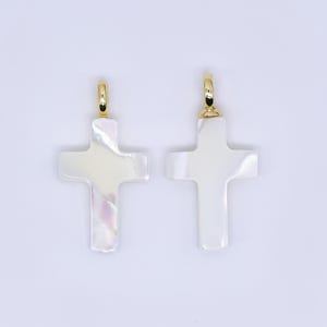 May include: Two cross pendants with a pearlescent finish. Each cross has a gold-colored bail at the top. The crosses are white with subtle iridescent hues. The background is a solid, light color.