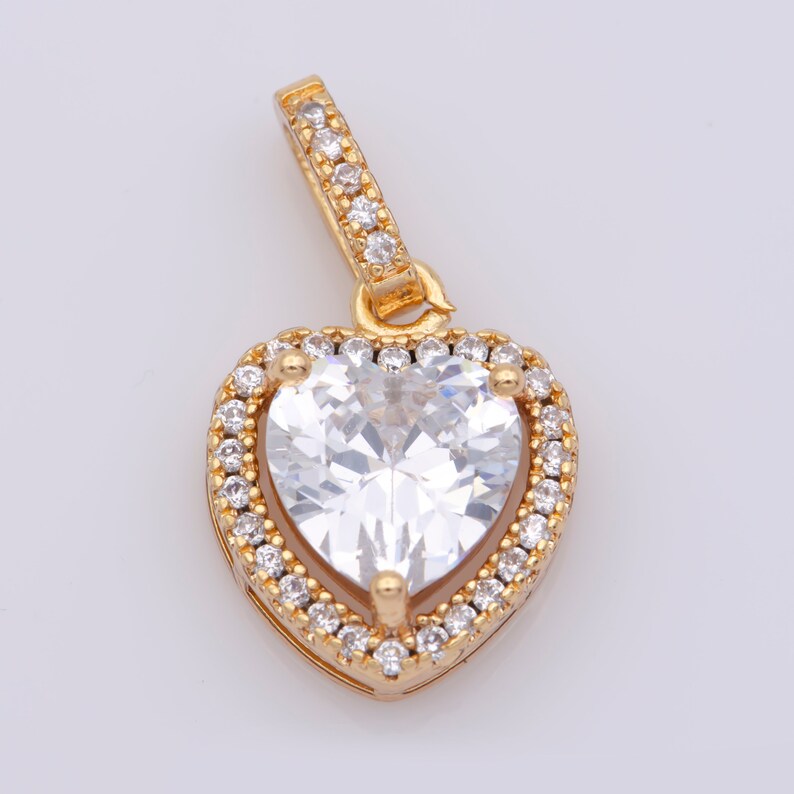 May include: A gold heart-shaped pendant featuring a large clear cubic zirconia stone surrounded by smaller clear cubic zirconia stones.