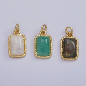May include: Three gold pendants with different colored stones. The pendants are rectangular with a gold border and a smooth, flat stone in the center. The stones are white, green, and gray.