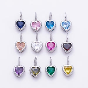 May include: A collection of twelve heart-shaped pendants arranged in three rows. Each pendant features a faceted gemstone in a different color, including blue, pink, light blue, peach, white, magenta, dark red, purple, olive, green, and yellow.