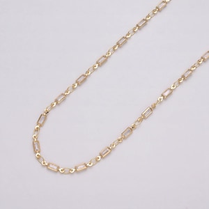 May include: A delicate gold-colored necklace with rectangular, clear crystal accents. The chain is composed of small, interconnected links, creating a refined and elegant accessory. The necklace is displayed against a plain, light background, highlighting its design.