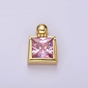 May include: A gold-toned pendant featuring a square-shaped pink gemstone set in a gold frame. The pendant has a small gold ball at the top for attaching to a chain.