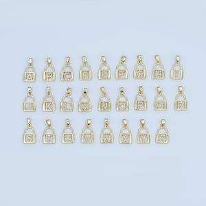 May include: Gold-colored initial letter pendants in a padlock design. Each pendant features a different letter of the alphabet, with clear crystals embedded within the letter and padlock frame. The pendants are displayed against a light background.