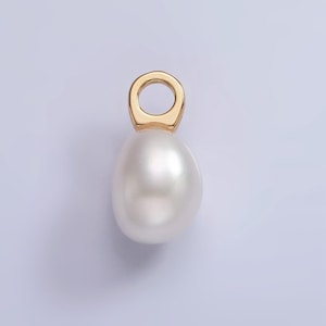 May include: A gold-colored pendant with a teardrop-shaped, lustrous white pearl. The pearl is connected to a circular gold bail. The pendant is set against a soft, light purple background.