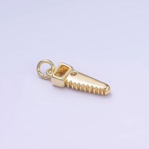 May include: Gold-toned saw charm pendant with a small clear stone detail. The charm is designed to look like a hand saw with a serrated edge.
