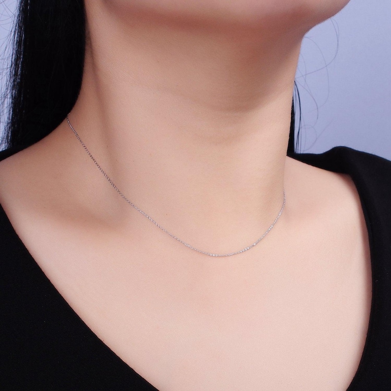 May include: A delicate silver chain necklace on a model wearing a black shirt.