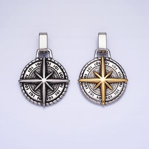 May include: Two silver compass pendants with a gold star design. The pendants are round and have a rope-like border. The star is in the center of the pendant and has eight points. The pendants are on a white background.
