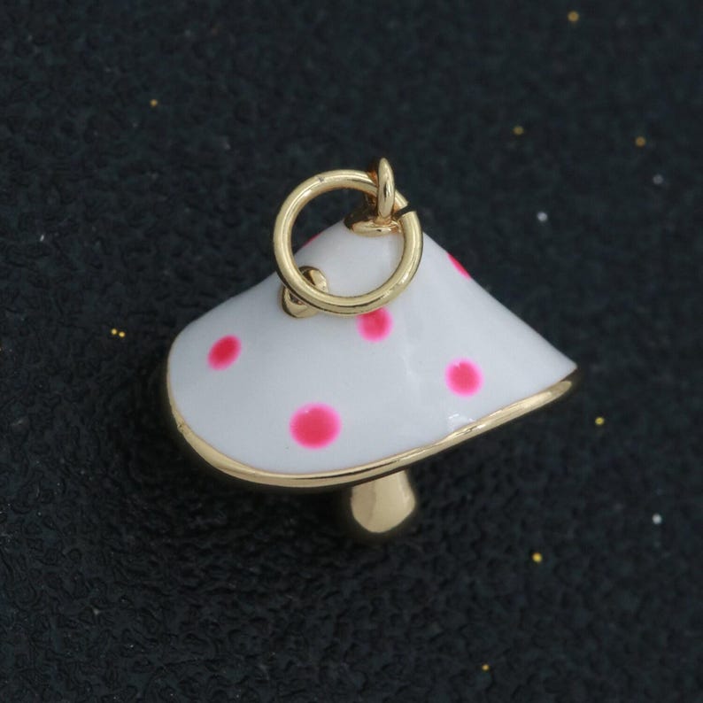 May include: A gold charm in the shape of a white mushroom with pink polka dots. The charm has a loop at the top for attaching to a necklace or bracelet.
