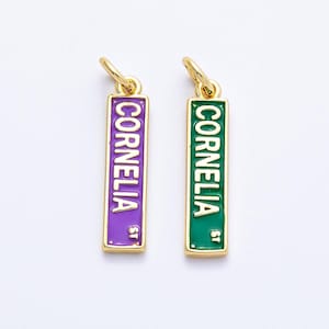 May include: Two gold-colored rectangular charms with the name "Cornelia" in white lettering. One charm has a purple background, the other is green. Both have a gold loop at the top for hanging.