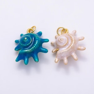 May include: Two seashell charms with gold-tone jump rings. One charm is a glossy, deep teal blue with a spiral texture, and the other is a pearlescent, pale cream color with a matching spiral design. Both feature multiple radiating points.