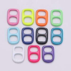 Puede incluir: Una colección de anillas de latas de refrescos de plástico de colores, en varios colores, incluyendo rosa, amarillo, naranja, verde, azul claro, azul oscuro, negro, turquesa, blanco, rojo y morado. Las anillas están dispuestas en filas y columnas.