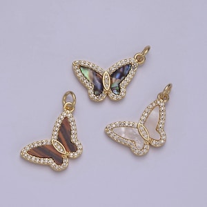 May include: Three gold-colored butterfly pendants with iridescent and pearl-like wings. Each butterfly is outlined with small, clear crystals. The pendants have a loop at the top for attaching to a chain or bracelet.