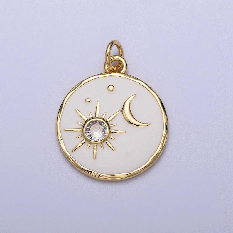 May include: Gold pendant with a white enamel circle featuring a sun with a clear crystal center, a crescent moon, and three small stars.